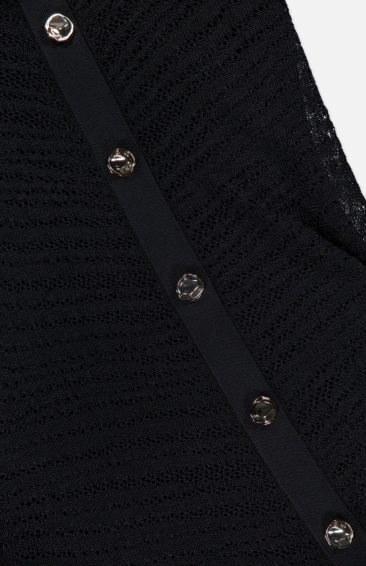 Close-up of the Zia Sheer Chevron Knit Dress by HEVRON, featuring black textured fabric, a diagonal strip with silver round buttons, and hints of a subtle chevron-zebra pattern.