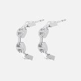 The HOORSENBUHS Micro Crescent Earrings feature interlocking tri-link chain motifs in silver, displayed on a light gray background—an elegant unisex jewelry choice.