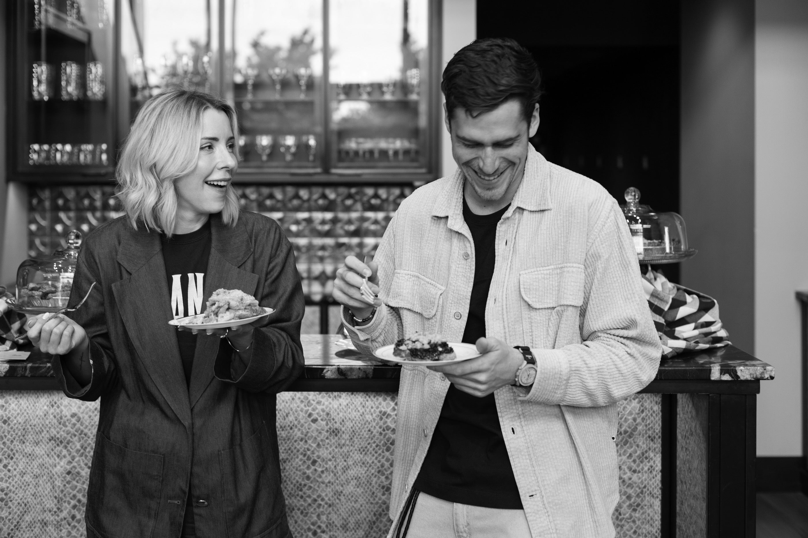 Two people standing in a bar or restaurant, holding plates with food.