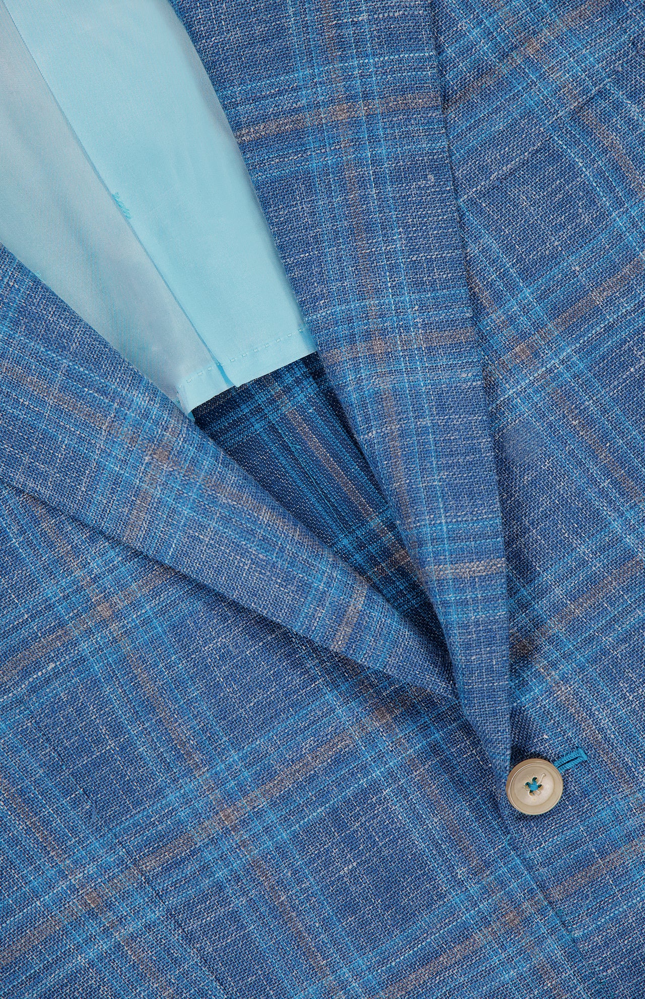 Close-up of ISAIA’s Check Light Summer Hopsack Sportcoat: men's blue plaid blazer with light blue and brown lines, a single tan button, and a light blue satin lining visible inside this Italian design.
