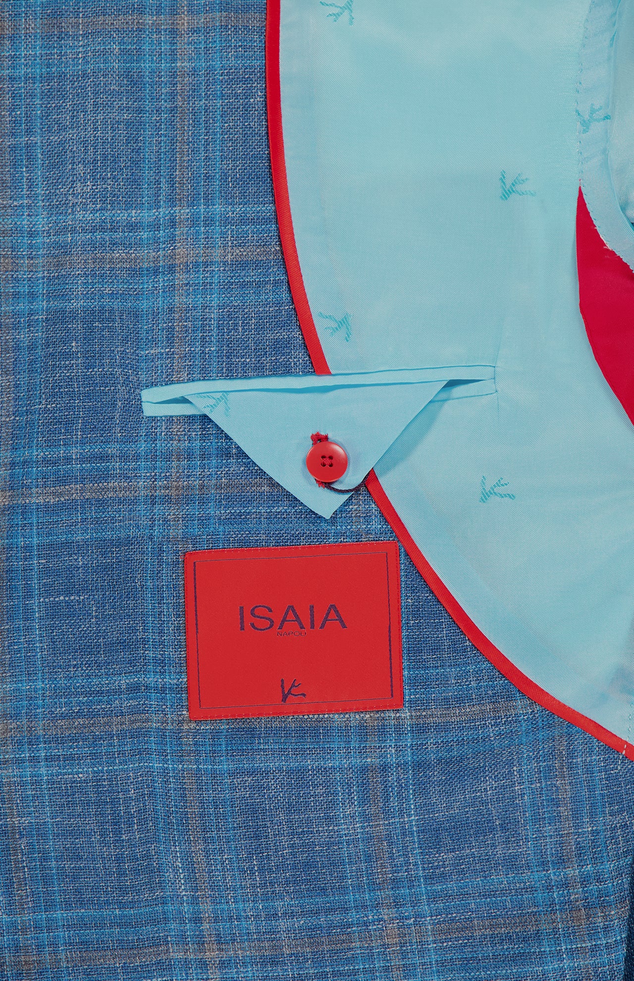 Close-up of the ISAIA Check Light Summer Hopsack Sportcoat, a men's blue plaid blazer with red-edged light blue lining, triangular flap with red button, and signature coral logo label—highlighting refined Italian craftsmanship.