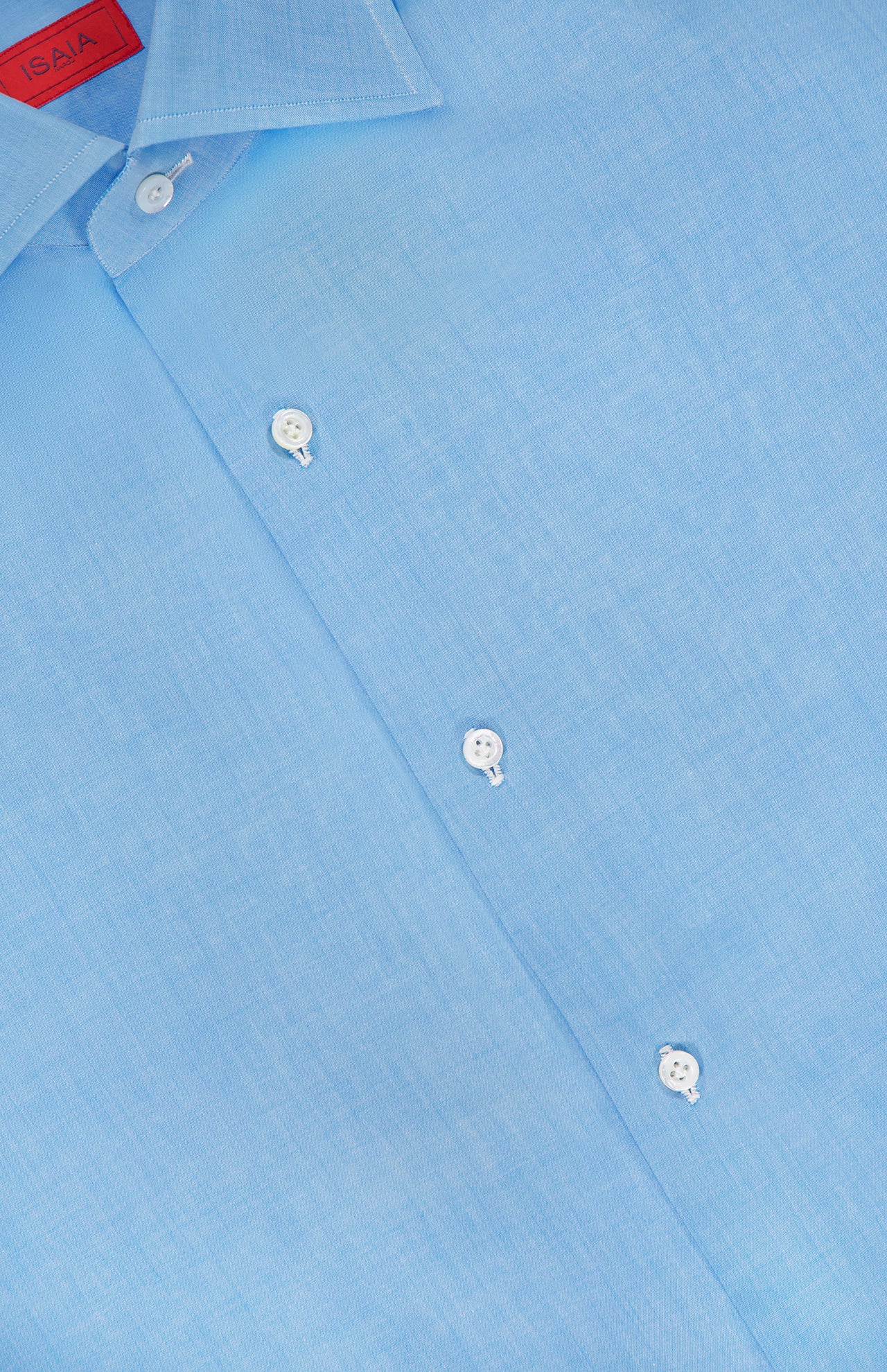 A close-up of the ISAIA Egyptian Cotton Dress Shirt in light blue shows white buttons, the collar, part of the placket, and a red label with white text inside the collar. Crafted from luxurious Egyptian cotton.