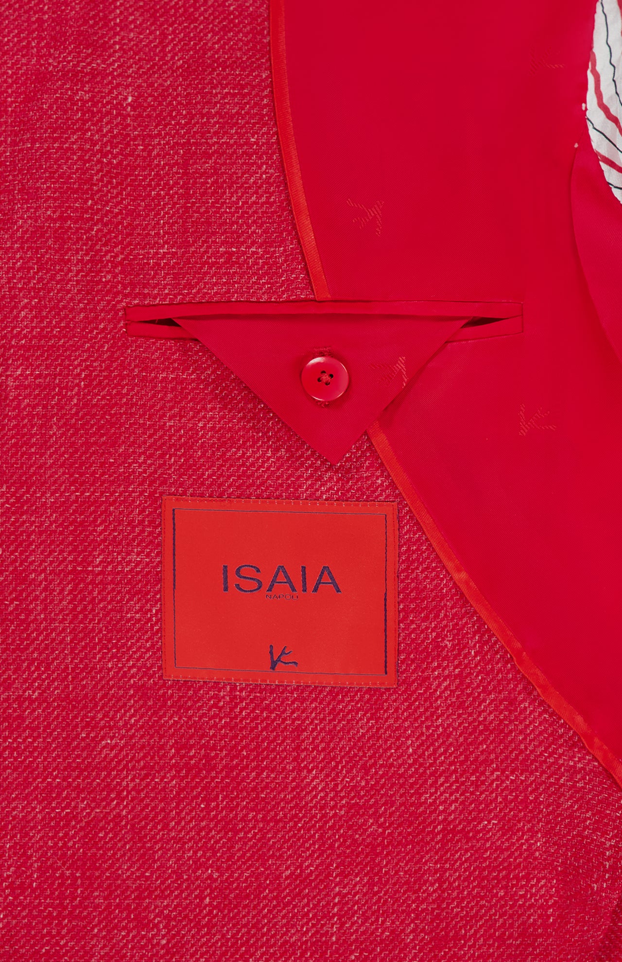 A close-up of the Cashsilk & Linen Sportcoat interior by ISAIA, featuring the brand label, a red button, and a triangular fabric flap. Detailed stitching and texture showcase Italian craftsmanship.