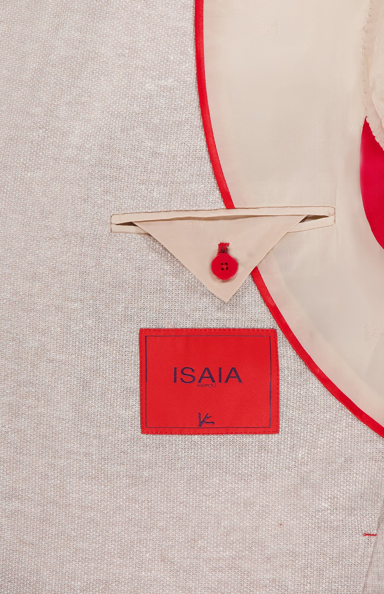 Close-up of the inside of an ISAIA Cotton Linen Jersey Sportcoat in beige with red trim, featuring a red brand label, tan pocket with triangular flap, and red button. Expertly crafted in Italy from a fine cotton-linen blend.