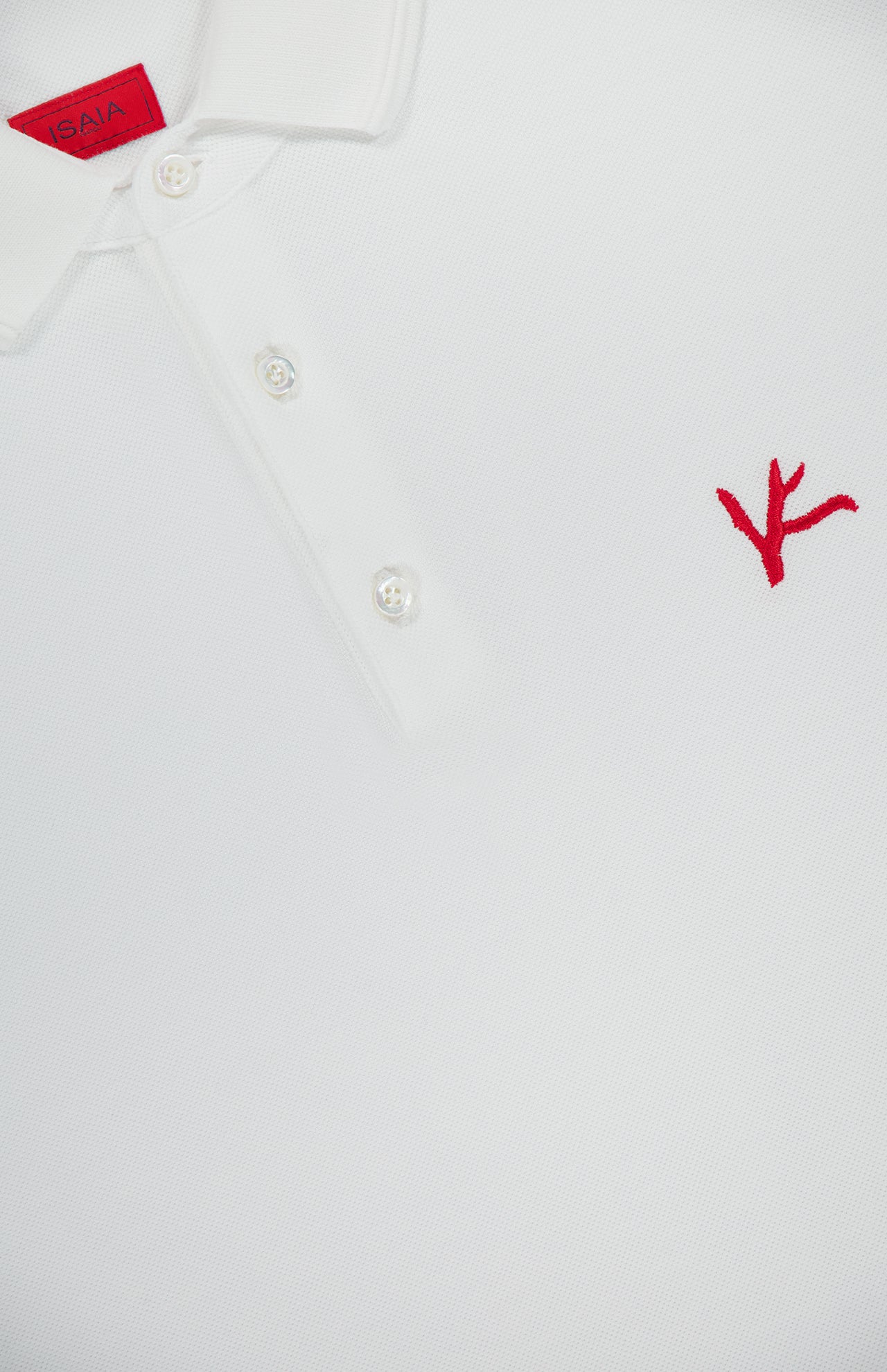 Close-up of the ISAIA Cotton Piquet Jersey Short Sleeve Polo Shirt in white, made in Italy with a classic three-button collar and red embroidered branch logo on the chest. A partially visible red tag is inside the collar.