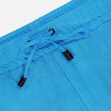 Close-up of the waistband on ISAIA's Drawstring Wide Leg Linen Corallo Trouser Pant, featuring bright blue linen, drawstring ties with black plastic tips, metal eyelets, a visible seam, and part of a pocket—perfect for vacation style.