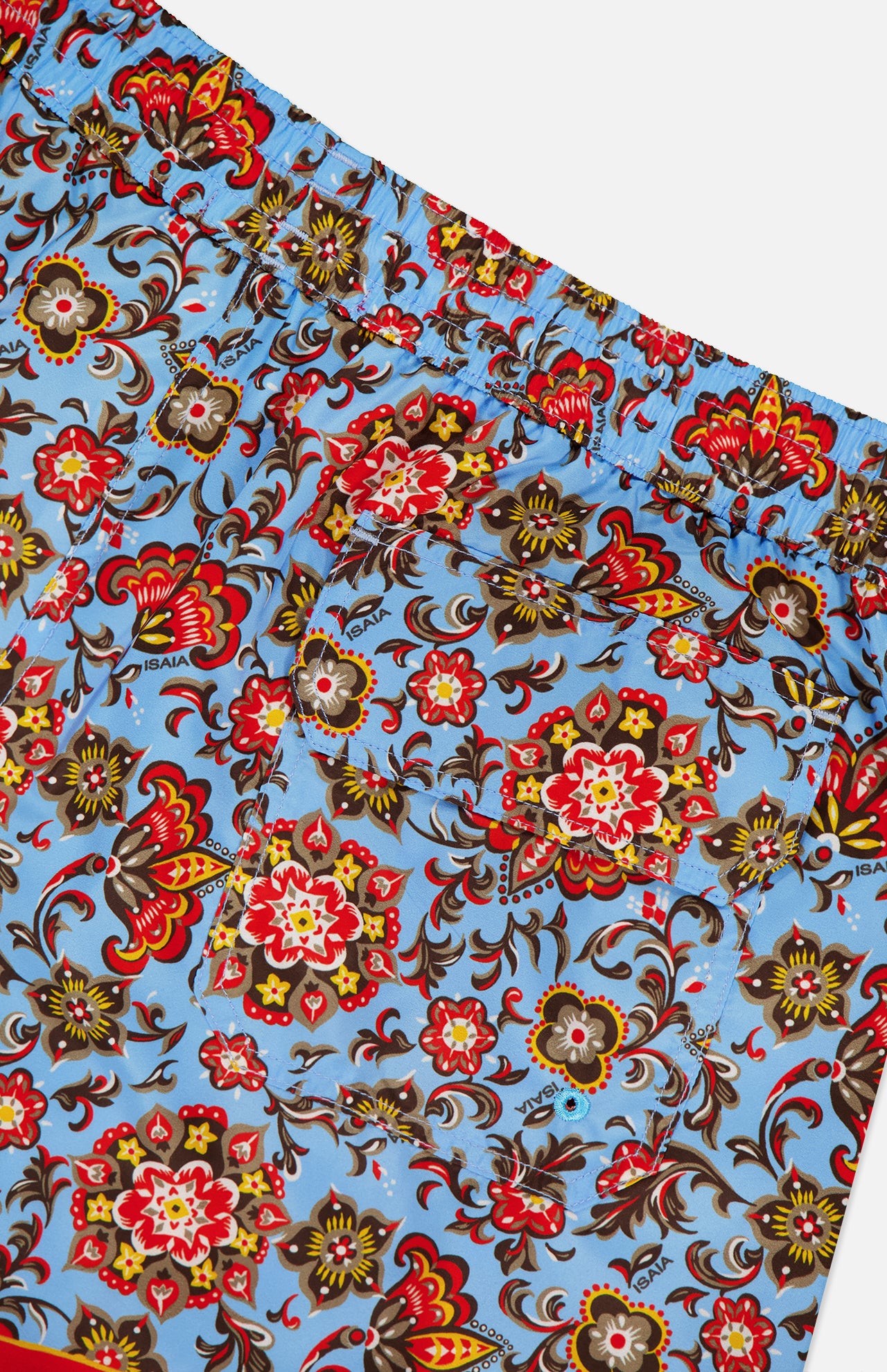 Close-up of ISAIA Drawstring Printed Swim Trunk: men's blue swimwear with a bold red, yellow, brown, and black floral print, elastic waistband, and back pocket.