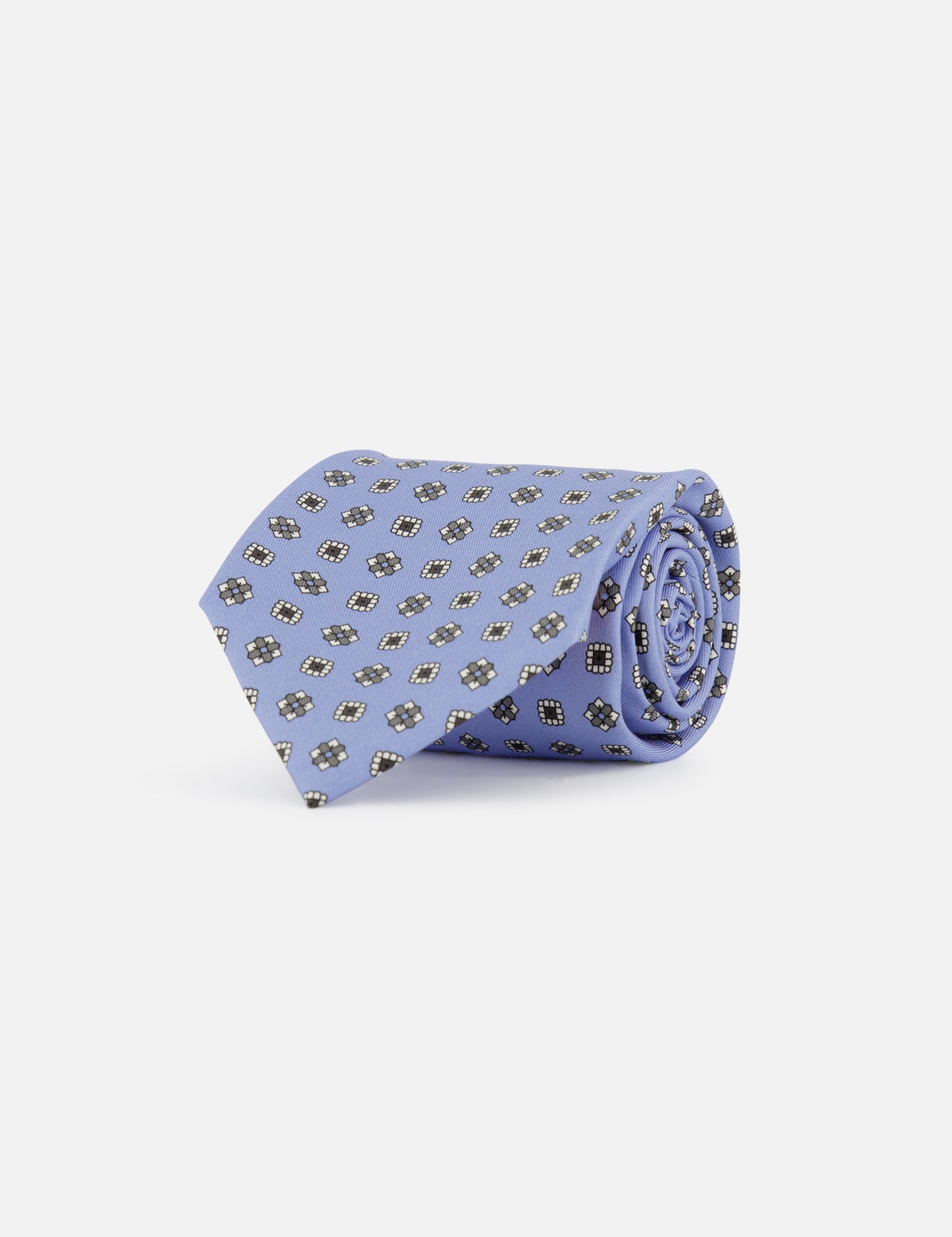 The ISAIA Floral Print Neck Tie, in light blue silk with a repeating black and white geometric pattern, is rolled up and displayed against a plain white background.