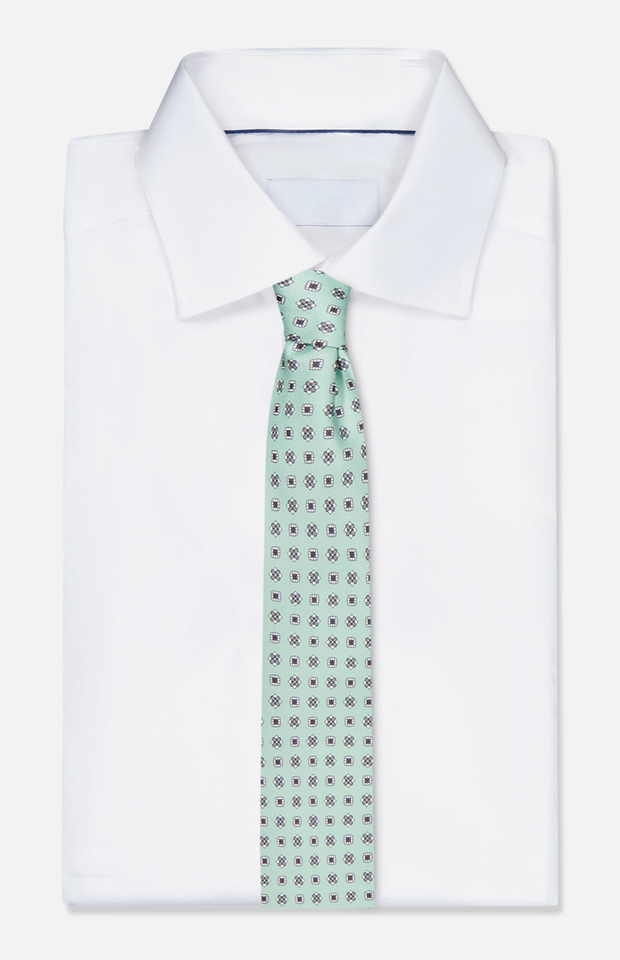 A white dress shirt is paired with the ISAIA Geometric Floral Print Tie, featuring a light green silk fabric adorned with small dark geometric floral designs, shown against a plain white background.