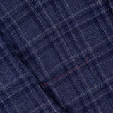 Close-up of the ISAIA Galles Over Check Rustic Sportcoat: a navy blue plaid wool-silk-linen blazer made in Italy, featuring intersecting light and dark lines, a button, and neatly sewn pocket. Fabric texture and weave are visible.