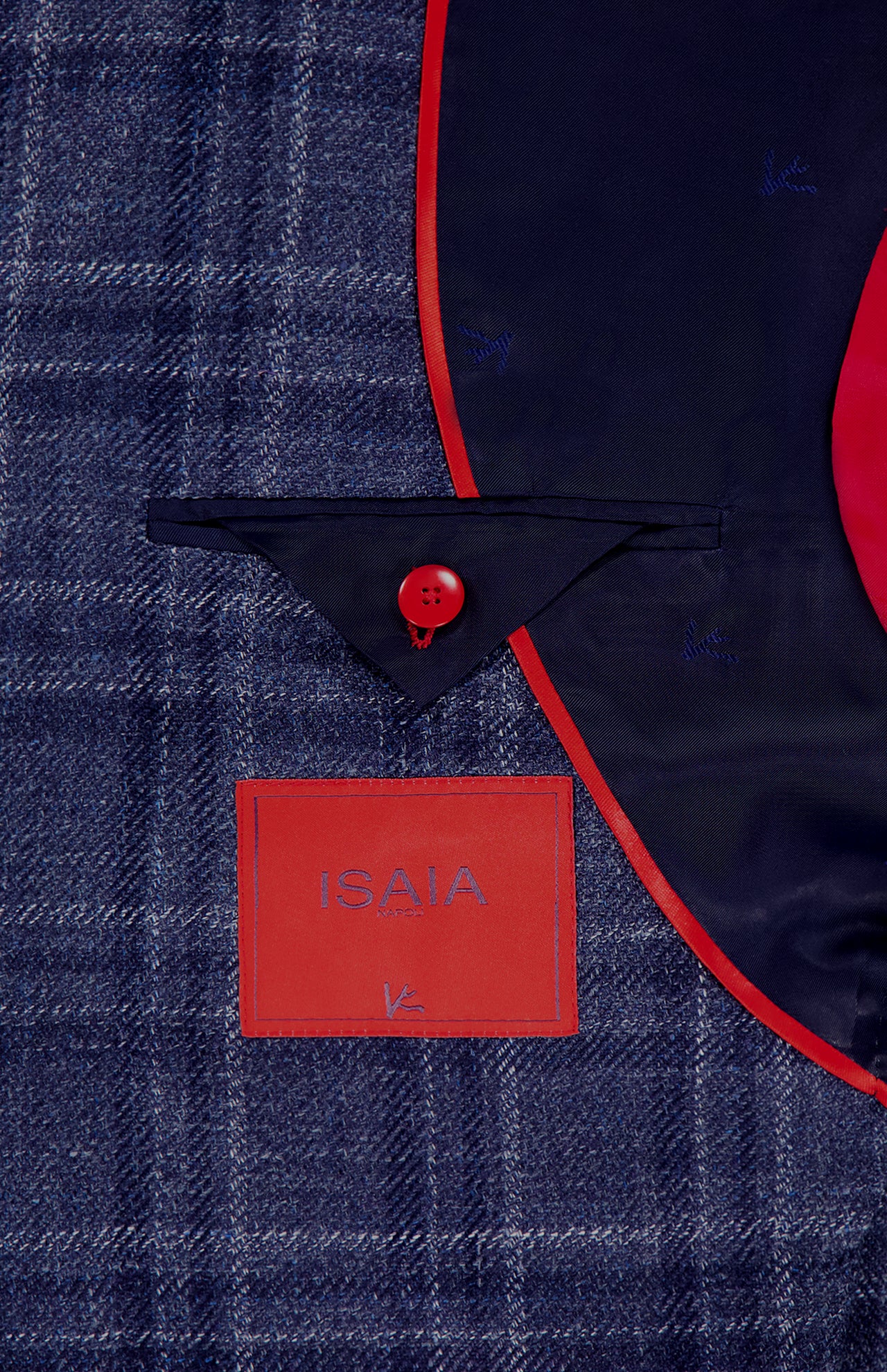 Close-up of the ISAIA Galles Over Check Rustic Sportcoat interior, featuring a red-edged pocket flap, red button, and red label on navy lining. The blue plaid fabric in the background highlights its made-in-Italy craftsmanship.