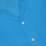 Close-up of the ISAIA Linen Coral Embroidery Shirt in bright blue, featuring a collar, white buttons, subtle coral embroidery, and a red brand tag inside the top left collar for a relaxed vacation look.