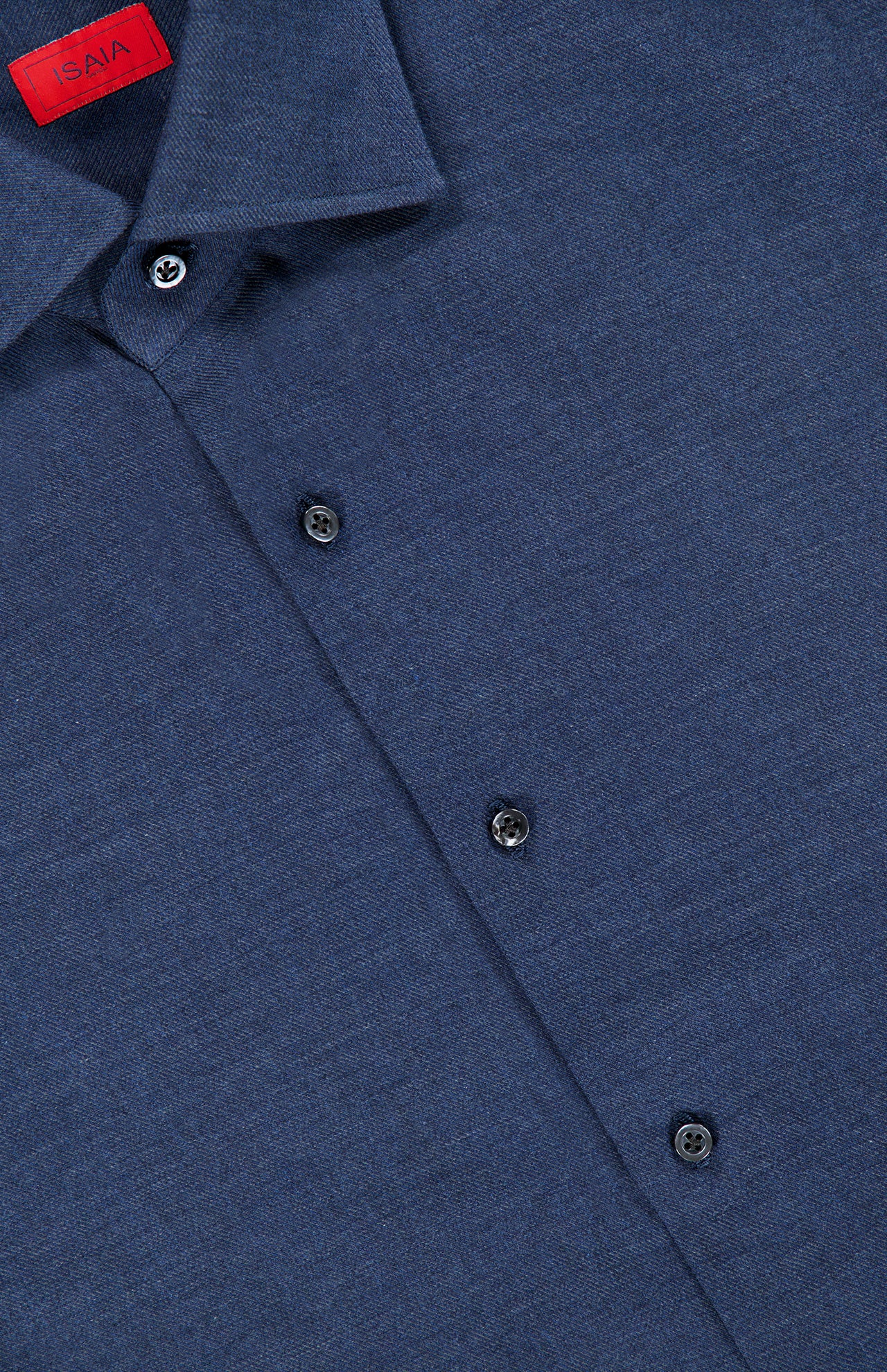 Close-up of the Lux Cashcotton Flannel Dress Shirt by ISAIA, featuring a blue hue with dark buttons and a signature red ISAIA label sewn inside the collar. The shirt’s smooth, subtly textured fabric highlights the refined elegance and expert craftsmanship characteristic of Italian dress shirts.