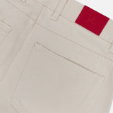 Close-up of the back pocket and waistband of ISAIA’s Napoli Stretch Denim Jeans in cream-colored cotton, featuring a bright red patch with an embossed logo on the waistband.