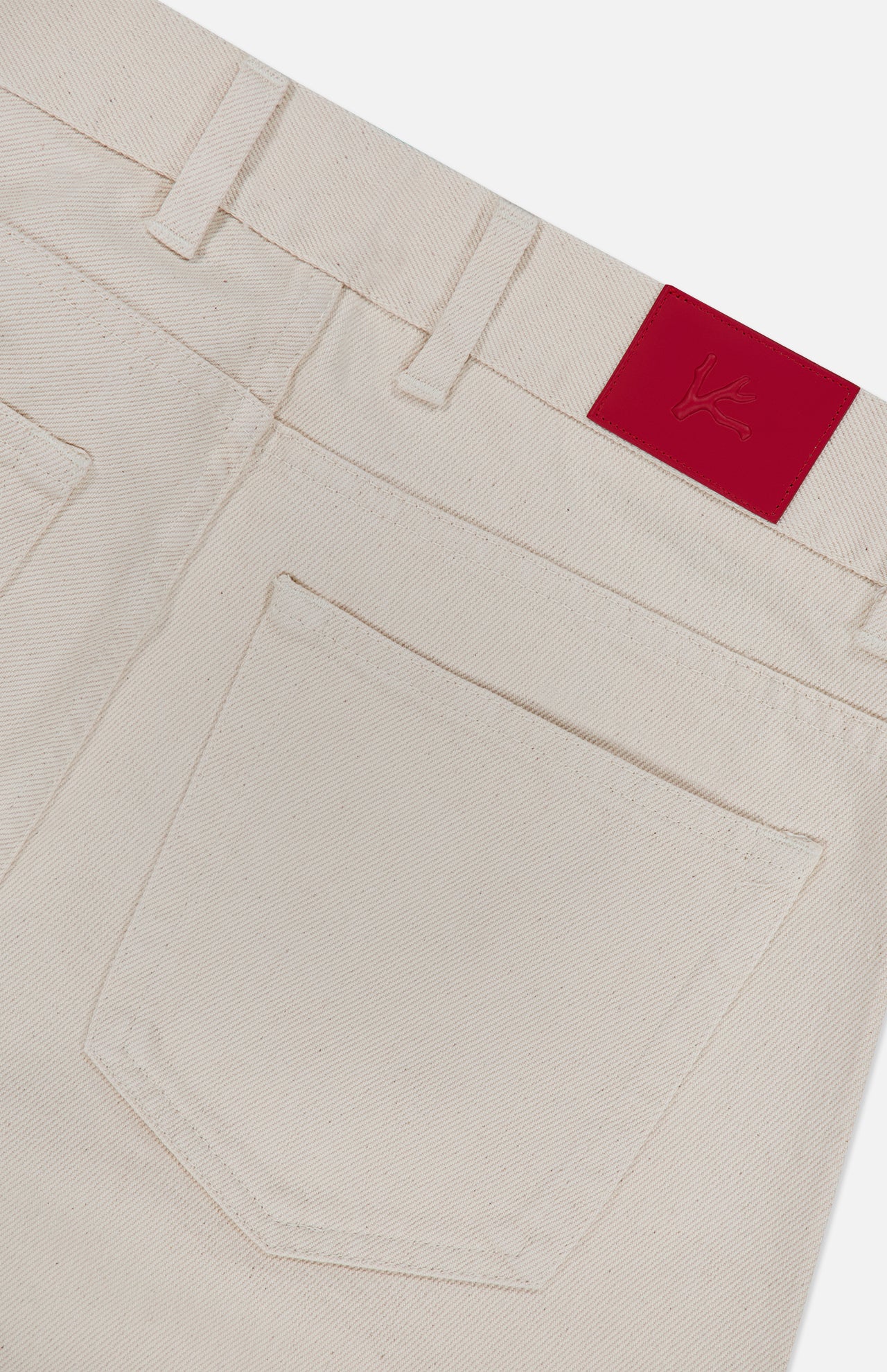 Close-up of the back pocket and waistband of ISAIA’s Napoli Stretch Denim Jeans in cream-colored cotton, featuring a bright red patch with an embossed logo on the waistband.