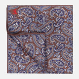 A Paisley Pocket Square by ISAIA, featuring a brown silk fabric with an elegant blue and white paisley pattern and a discreet red logo in the corner, is neatly folded against a plain background. Expertly crafted in Italy, this refined accessory exemplifies superior quality and classic style.