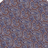 The Paisley Pocket Square by ISAIA is a brown silk accessory adorned with an intricate blue and white paisley pattern, featuring swirling teardrop shapes and floral motifs arranged diagonally. Expertly crafted in Italy, this elegant pocket square combines timeless design with superior craftsmanship.