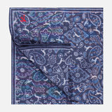 The ISAIA Paisley Pocket Square is a folded navy silk accessory, made in Italy, showcasing a blue, purple, and white paisley pattern with a small red embroidered logo in the corner.