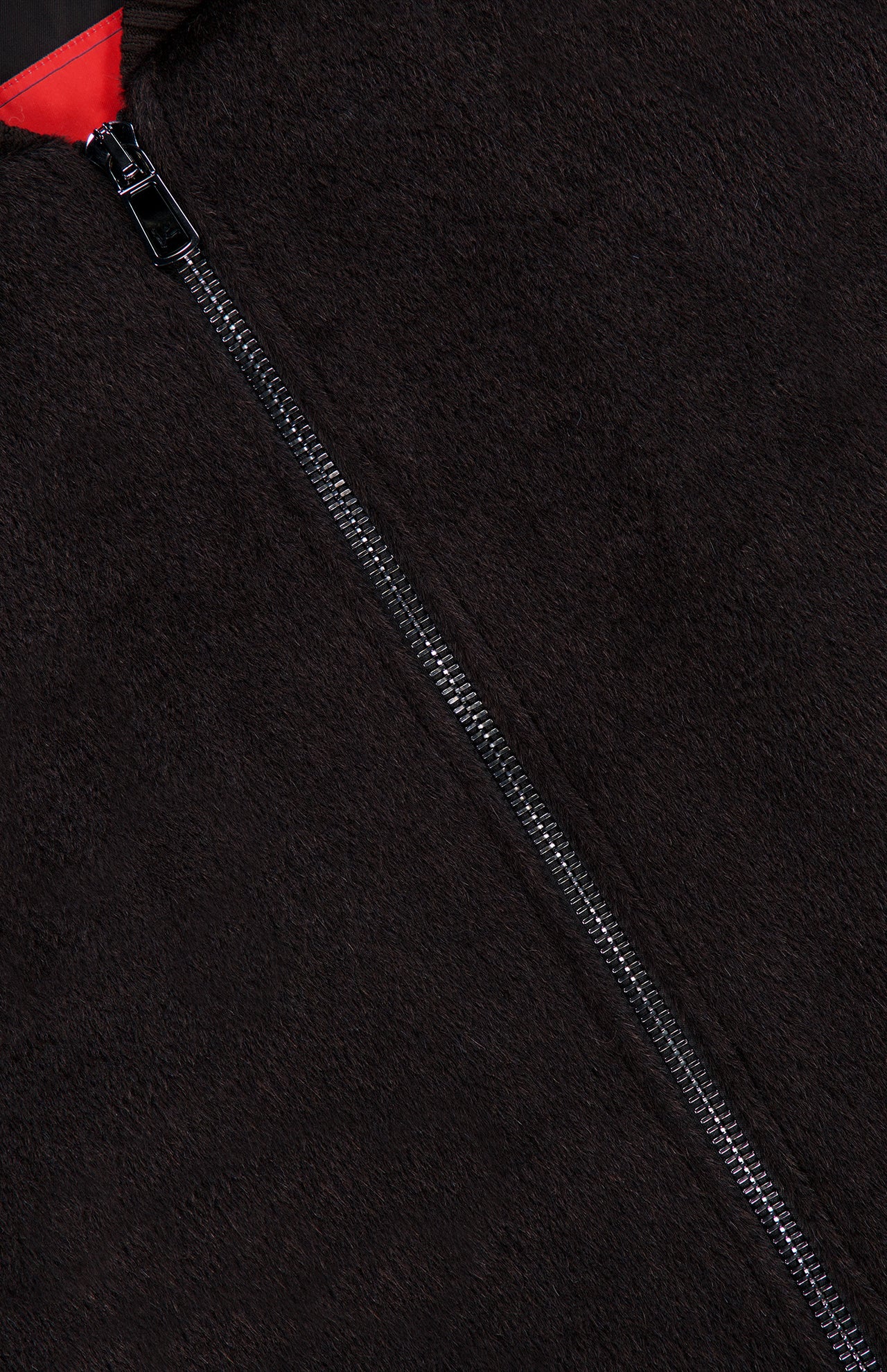 Close-up of a black fuzzy fabric with a central silver zipper, showcasing the luxurious texture of the ISAIA Peruvian Alpaca Varsity Bomber Jacket. A small section of red fabric appears near the top left corner beside the zipper, emphasizing the distinctive detailing characteristic of this premium men’s outerwear.