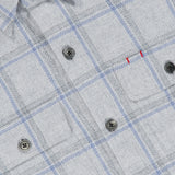 A close-up of the ISAIA Plaid Pastel Overshirt showcases its light gray fabric with blue plaid lines, black buttons, and a pocket adorned with two small red stitches. Soft and refined, this piece is expertly crafted in Italy.