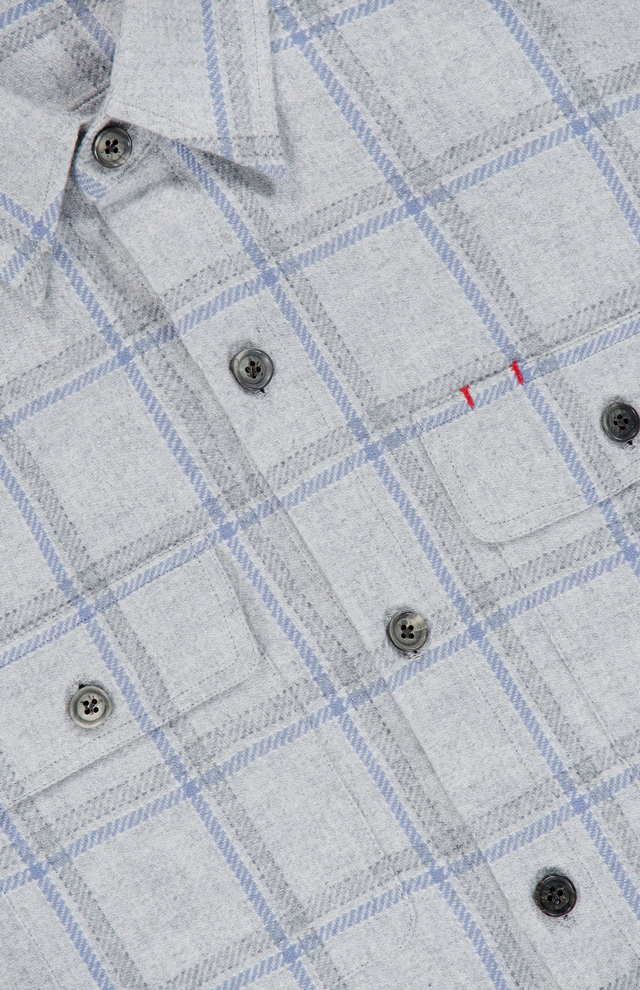 A close-up of the ISAIA Plaid Pastel Overshirt showcases its light gray fabric with blue plaid lines, black buttons, and a pocket adorned with two small red stitches. Soft and refined, this piece is expertly crafted in Italy.