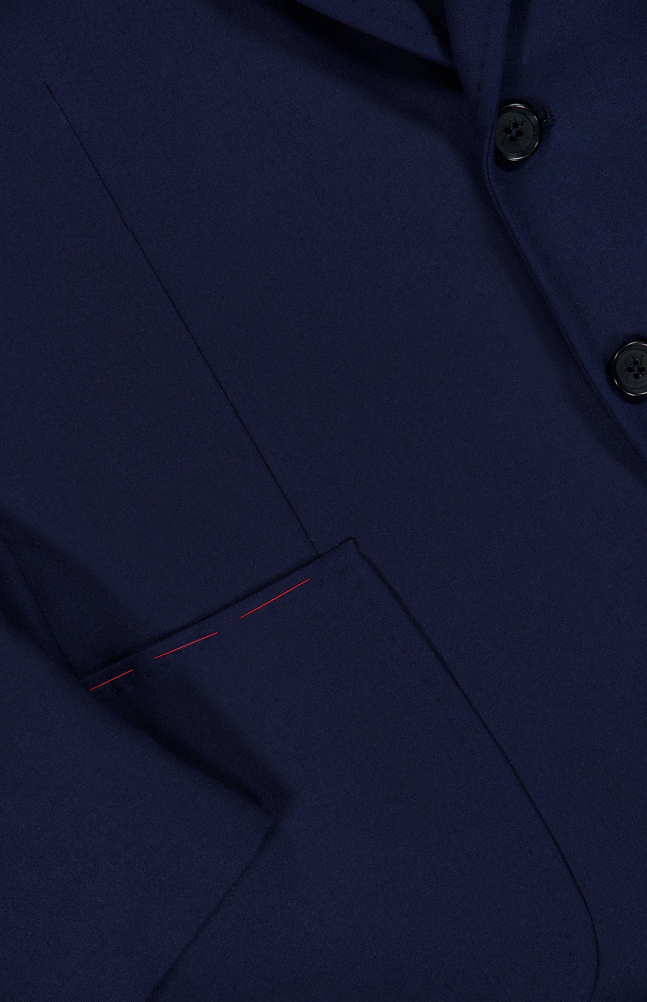 Close-up of the ISAIA Scuba Wool Comfort Suit Jacket in dark navy blue, featuring two black buttons and a front pocket with distinctive red stitching detail near the top edge.