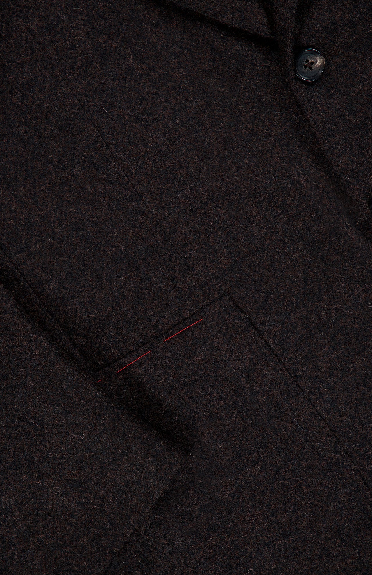 Close-up of the ISAIA Soft Boucle Alpaca & Wool Sportcoat, made in Italy. This dark brown jacket features a black button, lapel, and pocket accented with two short red stitches. The fabric is an alpaca wool blend with a textured boucle appearance.