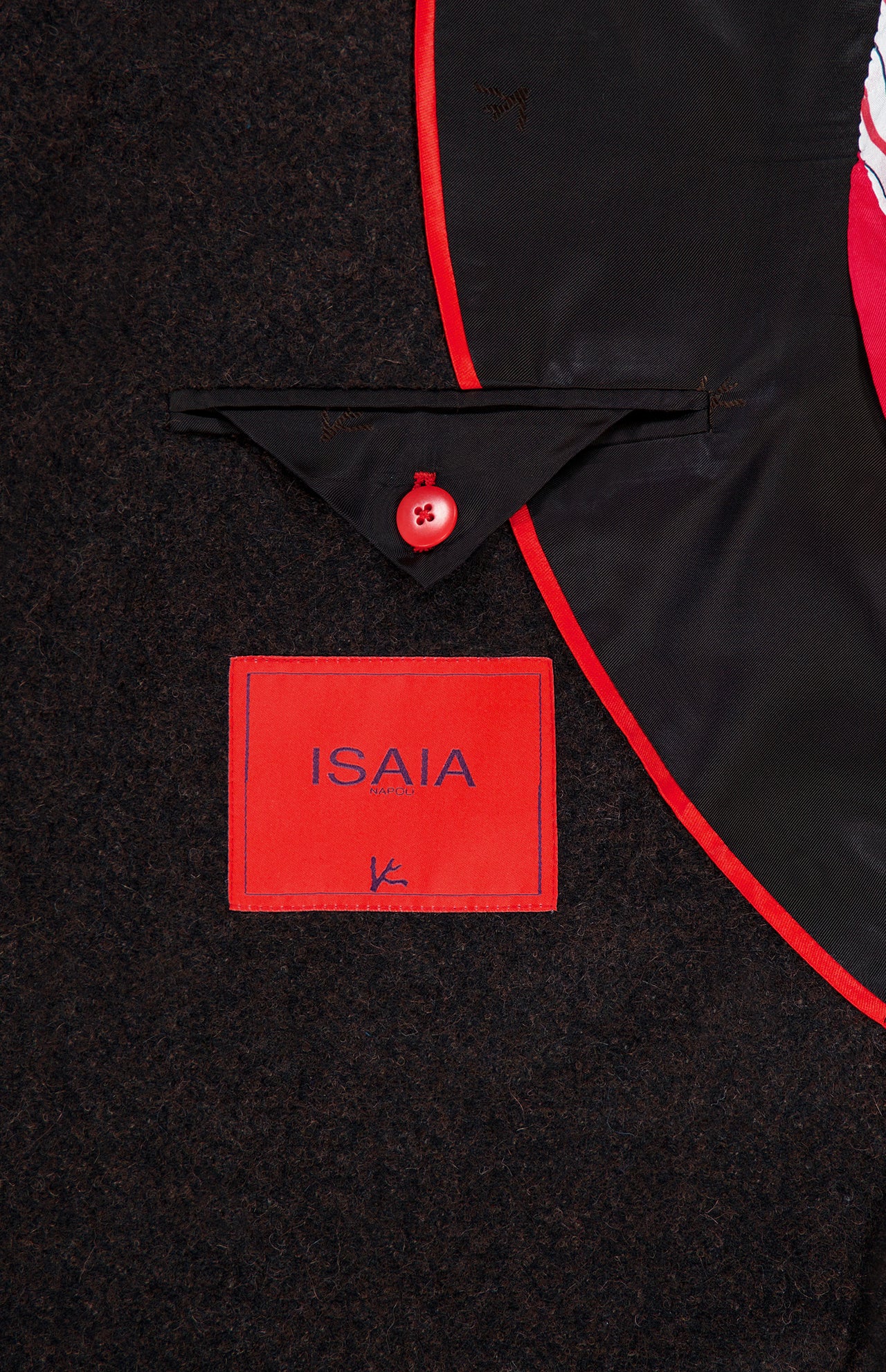 Close-up of the Soft Boucle Alpaca & Wool Sportcoat’s interior, showcasing a red ISAIA label, a triangular black flap with a red button, sleek black lining, and bold red piping. This expertly crafted ISAIA jacket is made in Italy from an alpaca wool blend.
