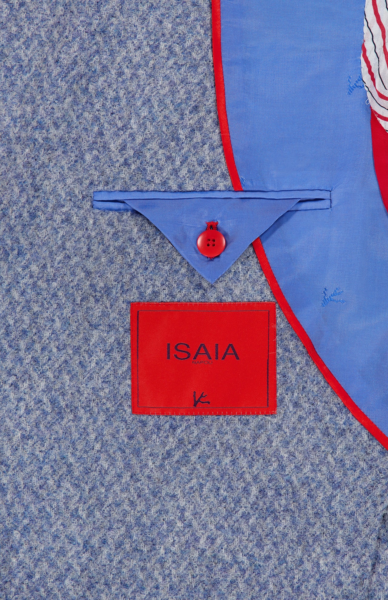 A close-up of the inner lining of the Soft Boucle Alpaca & Wool Sportcoat by ISAIA highlights its refined craftsmanship, featuring a red-bordered ISAIA label, a blue flap with a red button, and red piping along the edge—details that exemplify this Italian-made alpaca wool-blend jacket.