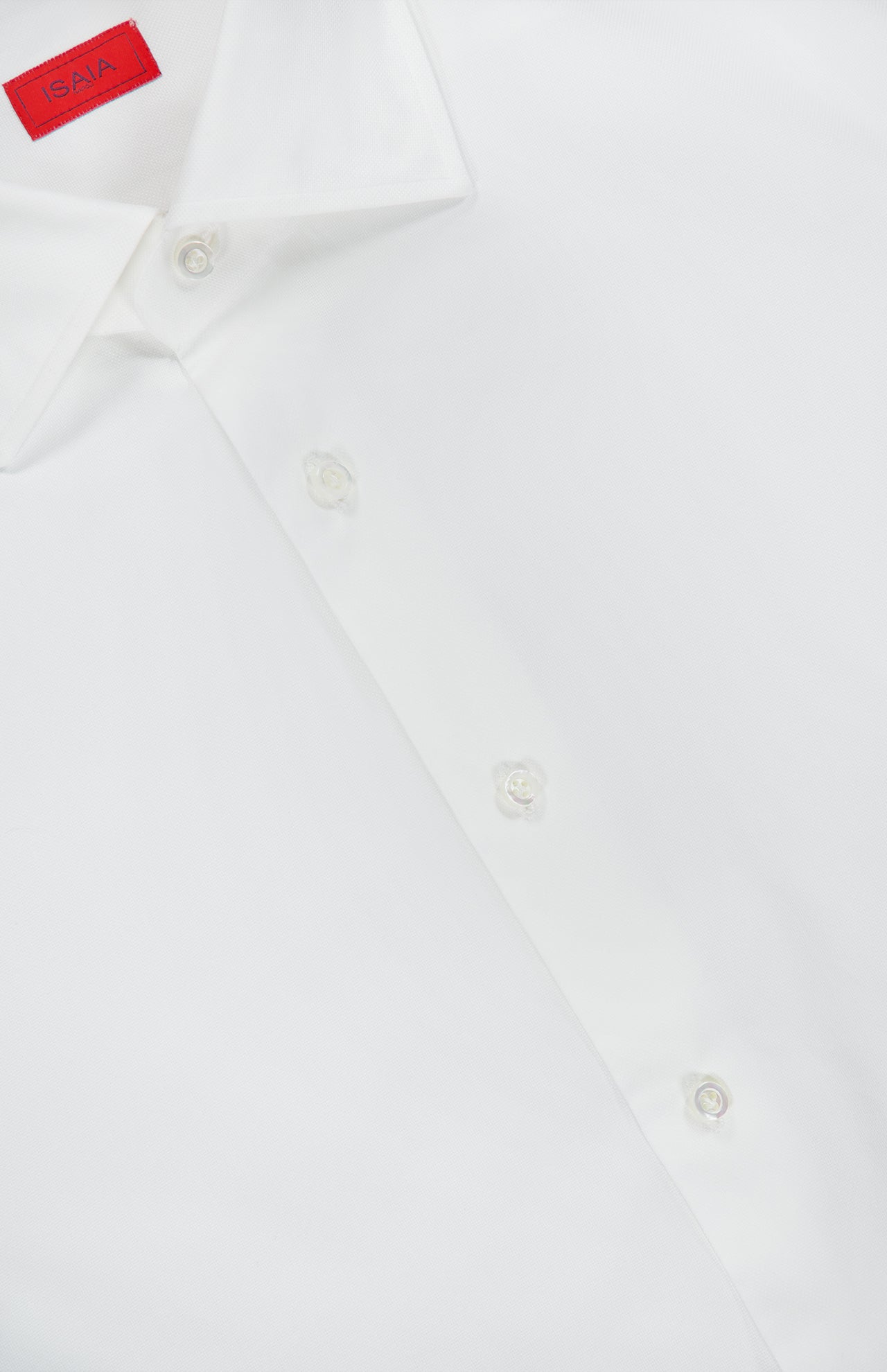 Close-up of the ISAIA Solid 2 Ply Dress Shirt, a white dress shirt with matching white buttons and a distinctive red label on the inside of the collar. This sophisticated Italian-made shirt exemplifies ISAIA’s renowned craftsmanship and timeless style, designed for those with discerning taste.