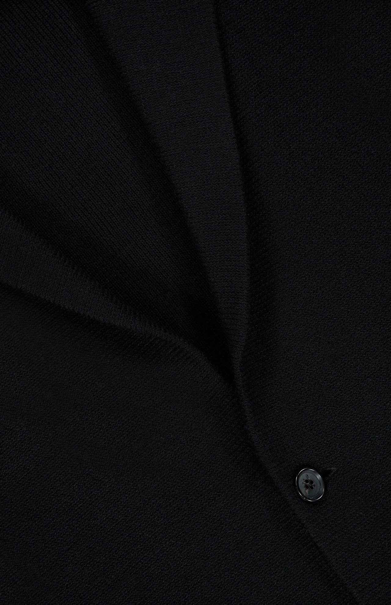 Close-up of black fabric from the ISAIA Two Button Knit Sportcoat, featuring a visible seam and a single black button. The texture of the knit fabric and detailed stitching are clearly shown, highlighting the garment’s quality craftsmanship.