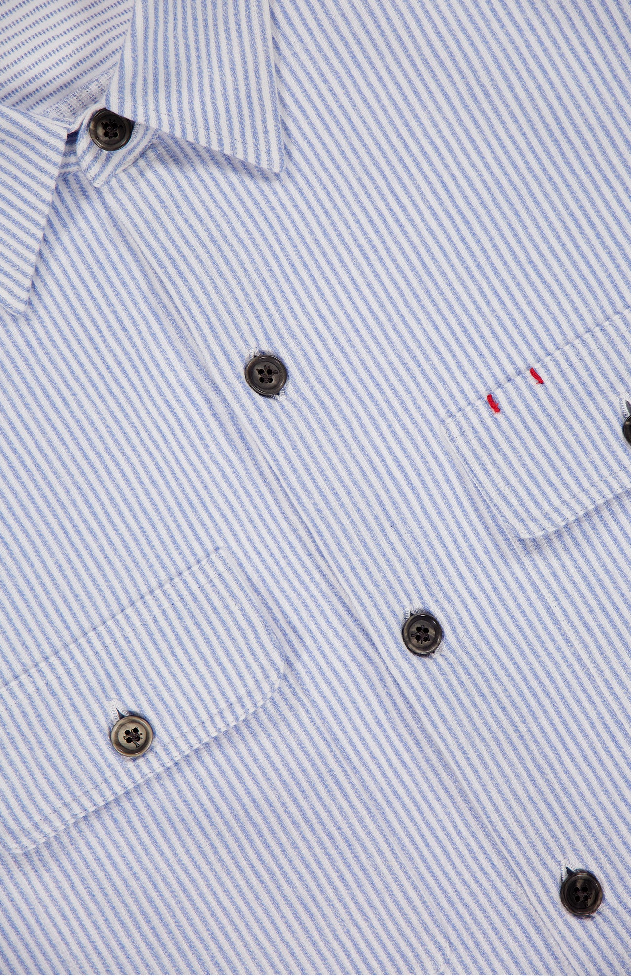 Close-up of the ISAIA Seersucker Effect Jersey Overshirt in light blue with black buttons and two chest pockets, one accented by subtle red stitching—the ideal piece for a nautical Italian summer look.