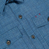 Close-up of the ISAIA Tela Mat Effect Overshirt featuring textured blue fabric, dark buttons, two chest pockets, a collar, and two small red stitches above the left pocket.