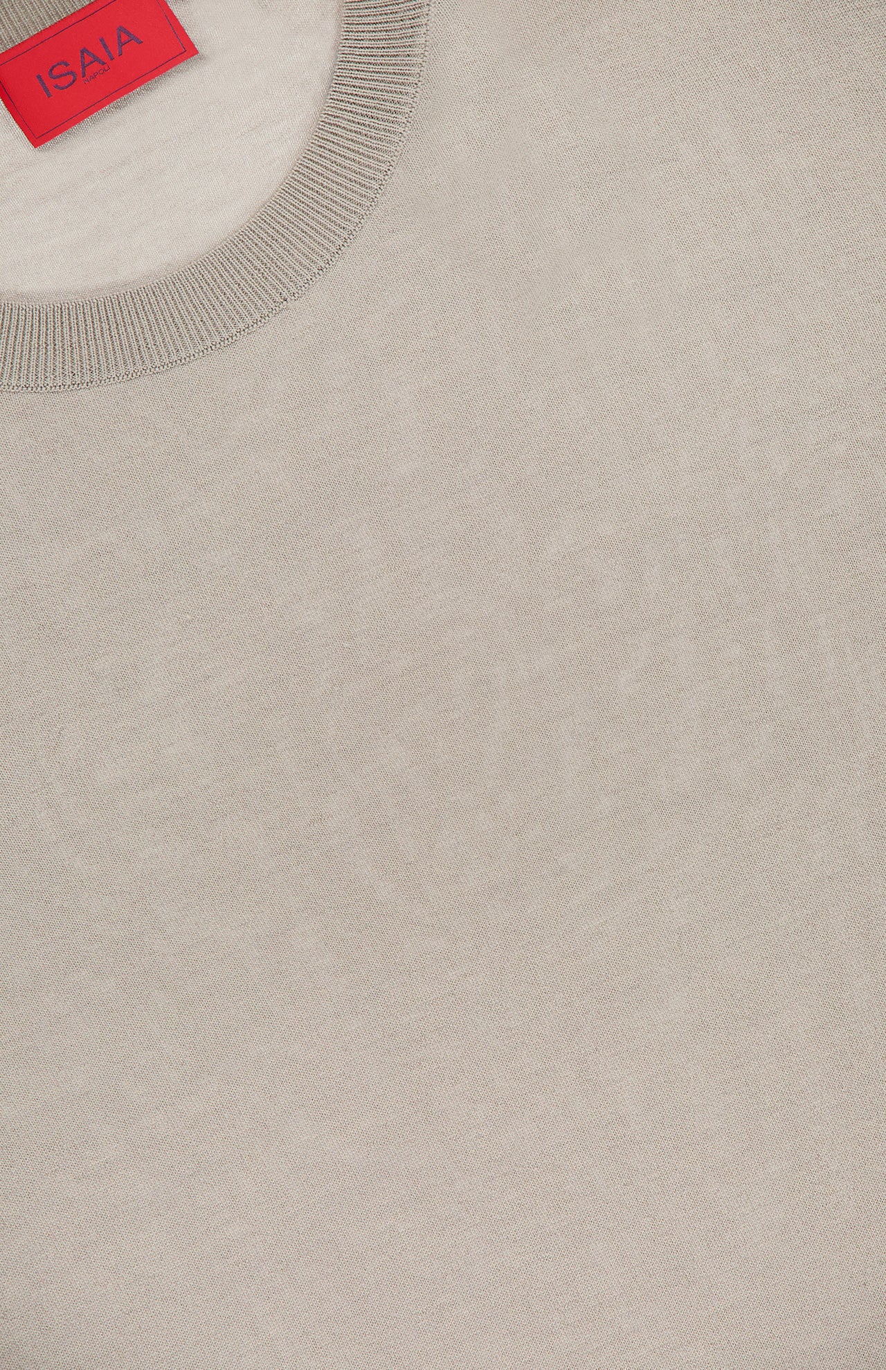 Close-up of an ISAIA Wool Cashsilk T-Shirt in light beige, featuring a ribbed crew neckline and crafted from luxurious wool, silk, and cashmere. A red ISAIA label is partially visible at the top left. Made in Italy.