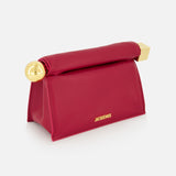 The JACQUEMUS La Pochette Rond Carre Clutch is a red, structured trapezoid bag with gold hardware on the corners and the brand's gold name on the front, embodying classic French elegance against a plain white background.