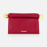 The JACQUEMUS La Pochette Rond Carre Clutch is a rectangular, deep pink French-style bag featuring a fold-over top, gold hardware at both ends, and JACQUEMUS in gold on the front—a bold designer statement for any event.
