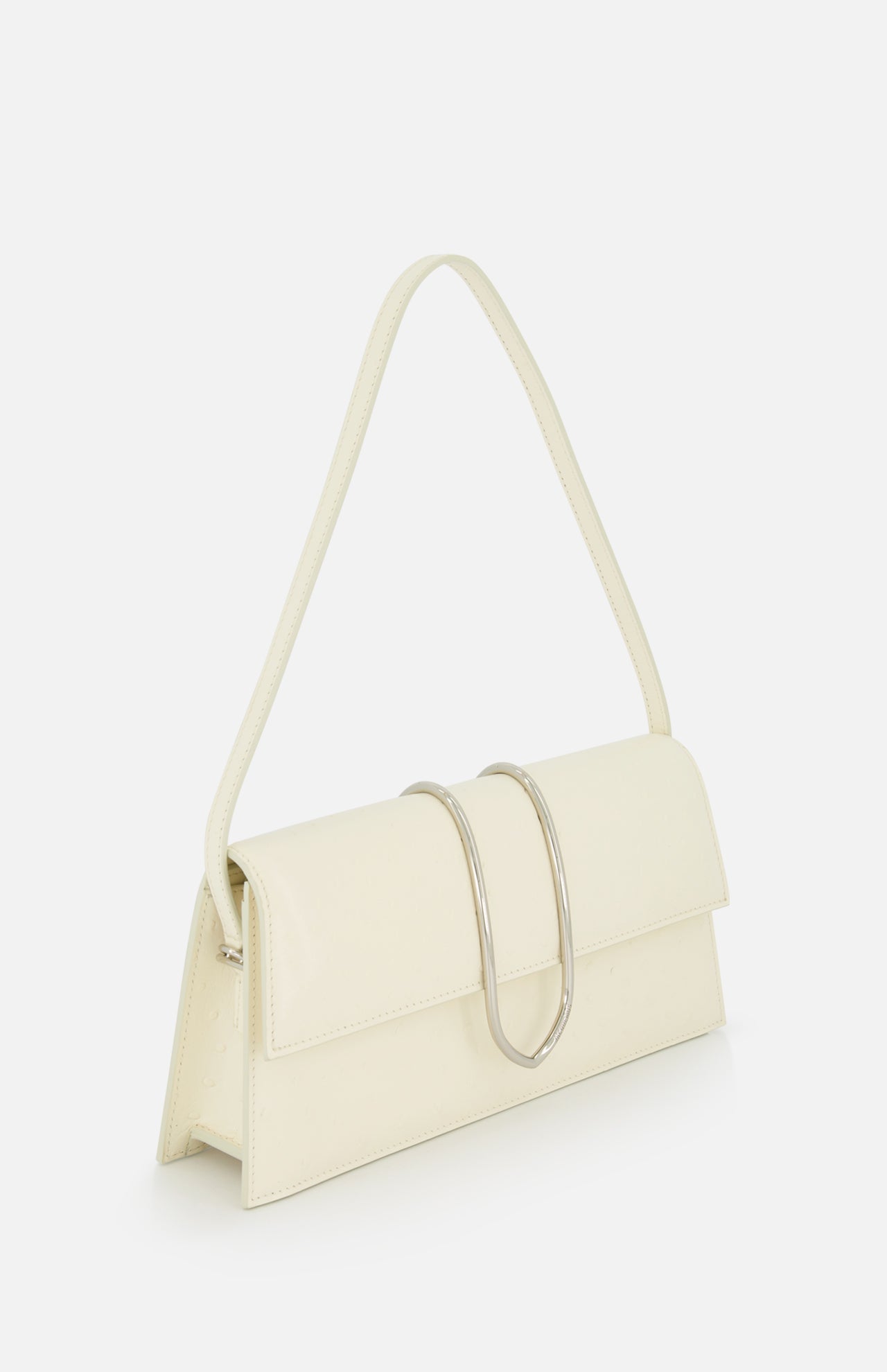 The JACQUEMUS Le Bambino Long Ostrich Bag is a cream-colored, off-white leather handbag made in Italy with a rectangular design, single shoulder strap, ostrich-embossed finish, and a large curved silver metal accent on the front flap.