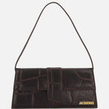 A rectangular, dark brown Le Bambino Long Croco-effect Shoulder Bag by JACQUEMUS with a single short strap and gold logo in the bottom right corner, set against a plain white background.