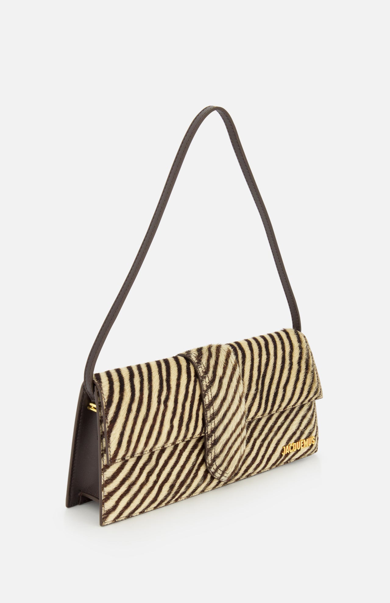 The JACQUEMUS Le Bambino Long Zebra Shoulder Bag is a rectangular shoulder bag made in Italy, crafted from luxurious calf hair with a zebra print pattern. It features a dark shoulder strap and is adorned with a gold Jacquemus logo on the lower right front corner, shown against a plain white background.