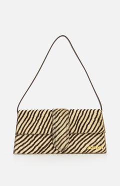 The Le Bambino Long Zebra Shoulder Bag by JACQUEMUS is a rectangular, zebra-print calf hair accessory featuring a short strap and gold JACQUEMUS branding in the lower right corner. Made in Italy, it is shown against a white background.