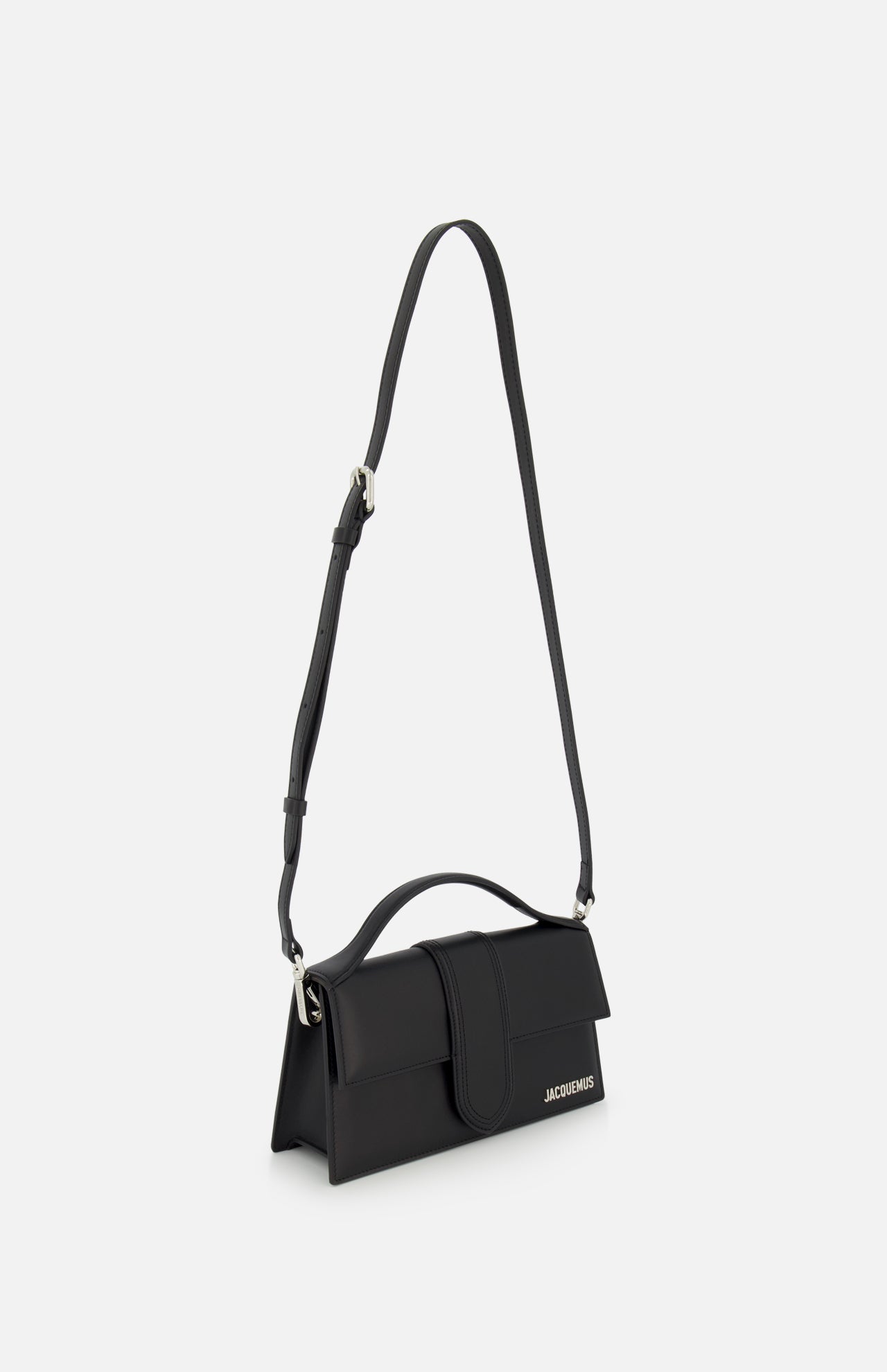 The Le Grand Bambino Bag by JACQUEMUS is a sleek black leather top-handle bag with an adjustable crossbody strap, flap closure, and the Jacquemus logo in small white letters on the front lower corner. Made in Italy.