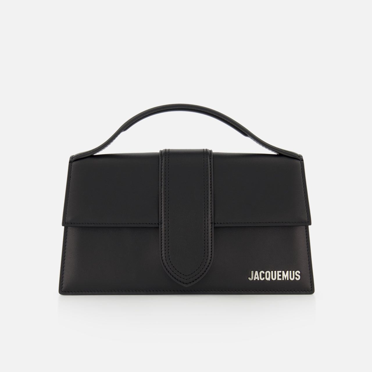 The Le Grand Bambino Bag by JACQUEMUS is a black leather top-handle bag with a flap closure, adjustable crossbody strap, and the JACQUEMUS logo in white on the lower right—made in Italy and shown against a white background.