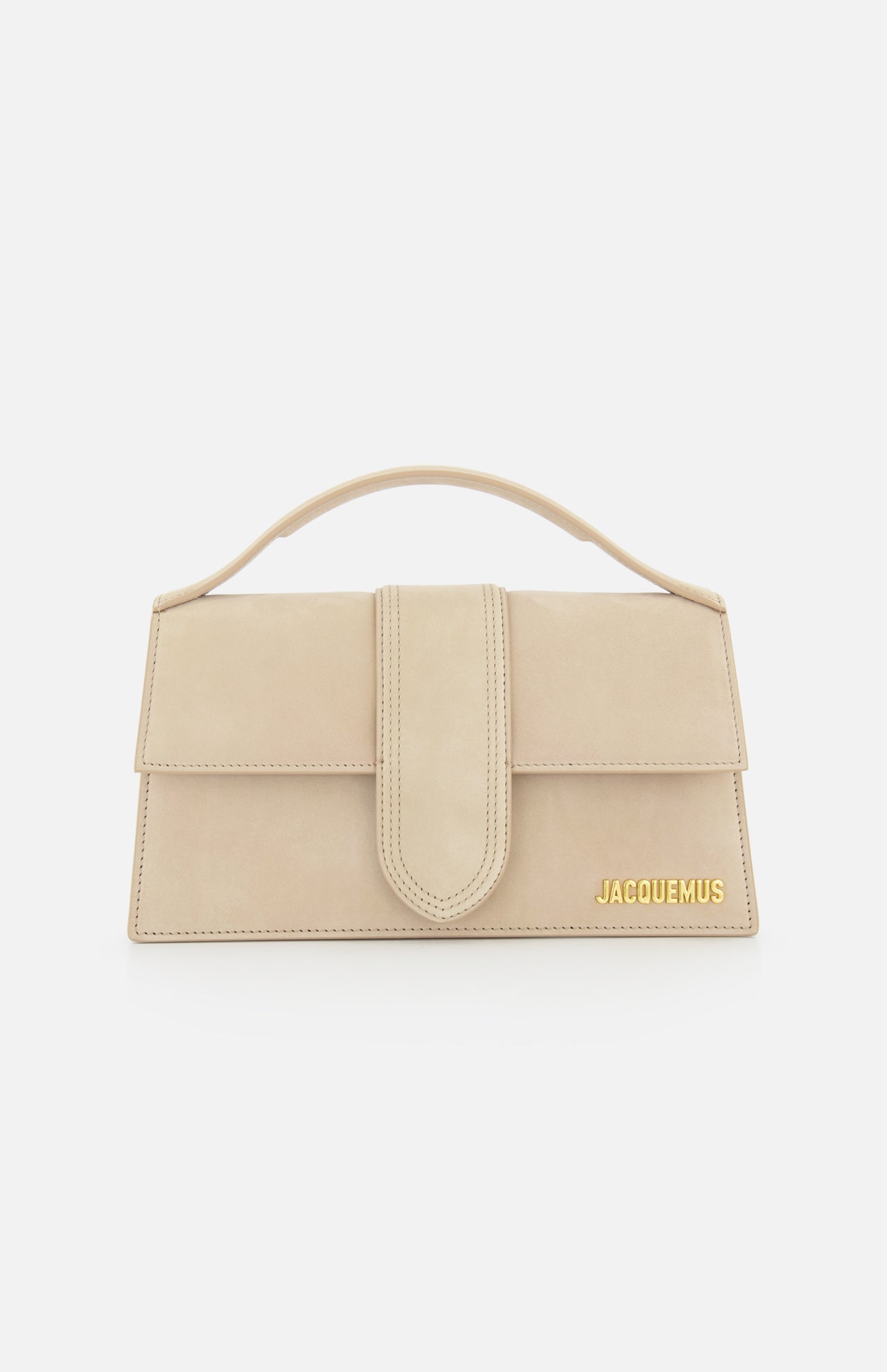The JACQUEMUS Le Grand Bambino Bag is a tan leather top-handle bag made in Italy, featuring a front flap closure and gold logo at the bottom right corner, shown against a white background.