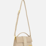 The JACQUEMUS Le Grand Bambino Bag is a tan leather top-handle bag with gold accents, crafted in Italy and featuring an adjustable crossbody strap for versatile styling.