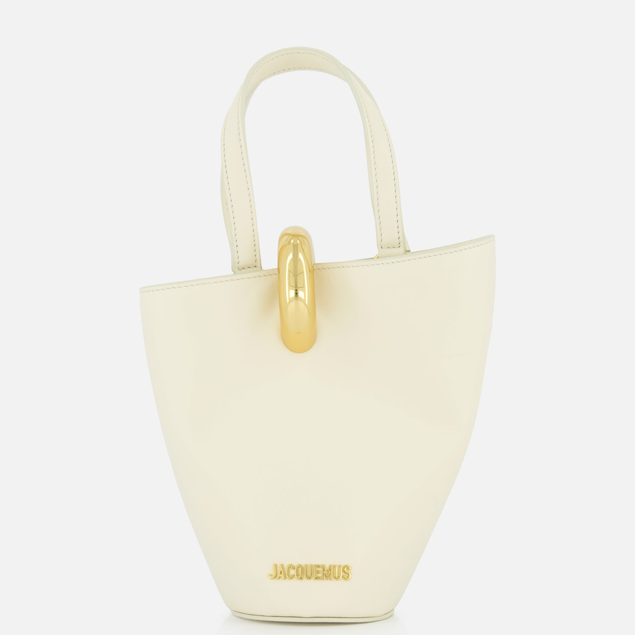 The Le Petit Bambola Tote Bag by JACQUEMUS is a small, structured off-white handbag with dual handles, gold hardware, and “JACQUEMUS” in gold lettering on the front for a minimalist, elegant look.