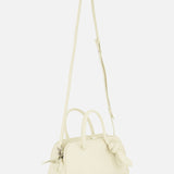 The JACQUEMUS Le Petit Turismo Bowling Bag is a small, off-white leather accessory with two handles, an adjustable strap, zipper closure, and a knotted detail—capturing quiet luxury against a plain white background.
