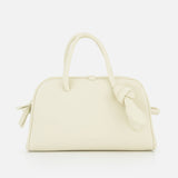 The Le Petit Turismo Bowling Bag by JACQUEMUS is a small, off-white leather accessory with two top handles and a side knotted strap, embodying quiet luxury against a plain white backdrop.