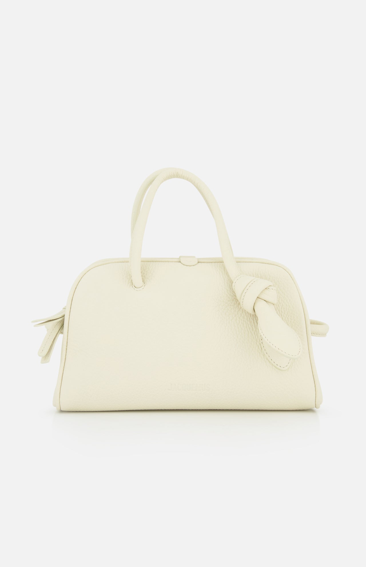 The Le Petit Turismo Bowling Bag by JACQUEMUS is a small, off-white leather accessory with two top handles and a side knotted strap, embodying quiet luxury against a plain white backdrop.