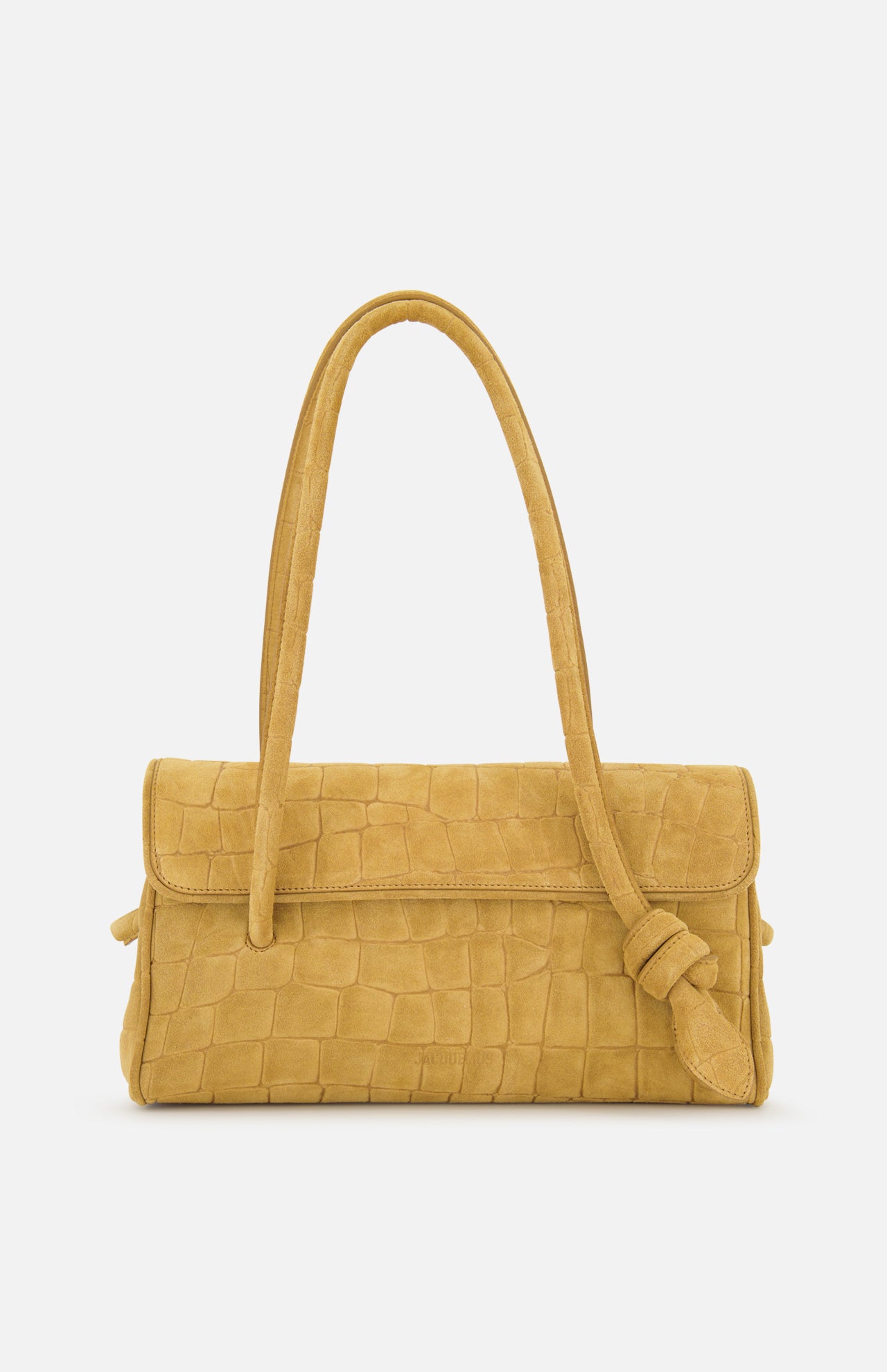 The Le Turismo Long Shoulder Bag by JACQUEMUS—a tan croc-effect suede handbag in a mustard yellow hue, crafted in Italy with a textured crocodile-style pattern, sophisticated flap closure, and a single knotted shoulder strap—is elegantly displayed on a white background.