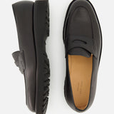 The Lopez Gentle Grain Loafer by JOHN LOBB is showcased against a white background, featuring one black leather loafer handmade in England displayed from the side to highlight its textured sole, while the other is shown from above to reveal the tan insole and sleek design.